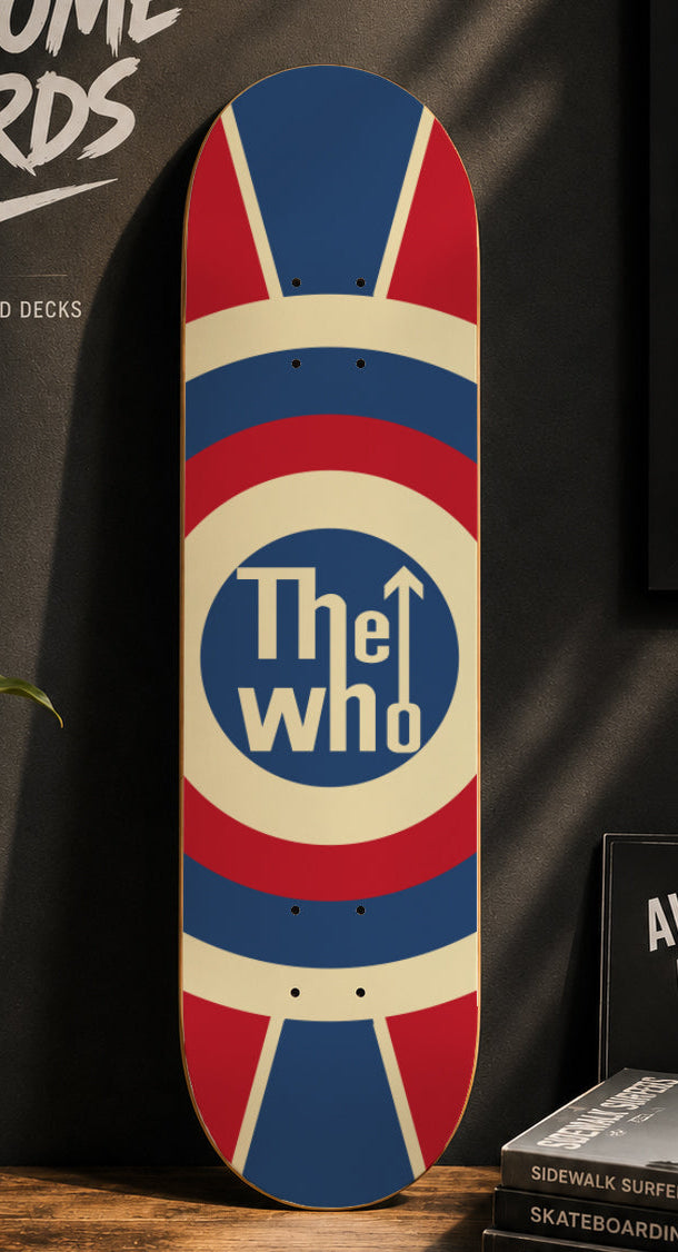 A skateboard deck leaning against a dark wall in a styled indoor setting. The deck features a Union Jack-inspired design with red, white, and blue quadrants and a central blue circle containing the text 'The who' with an upward arrow.